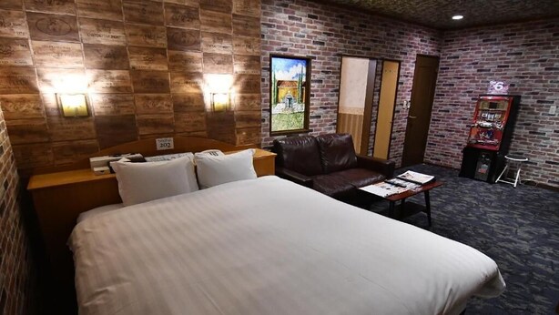 A hotel room with a large bed, a leather sofa, a small table, and a wall-mounted TV. - hotel dolphia – Adults Only (Daisen)
