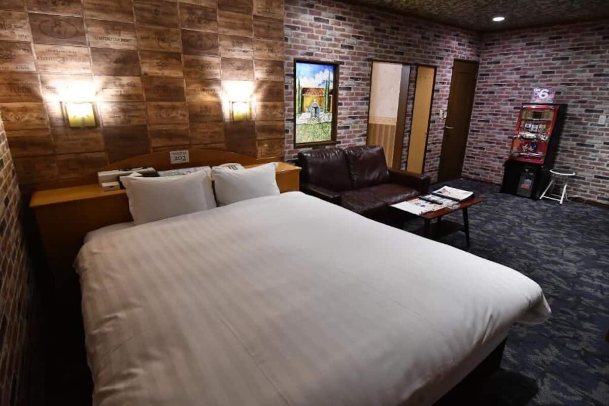 Habitación de hotel con una cama grande, un sofá de cuero, una mesita y un televisor instalado en la pared.