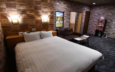 A hotel room with a large bed, a leather sofa, a small table, and a wall-mounted TV.
