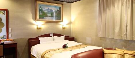 A hotel room with a bed, a red leather sofa, a painting on the wall, and a window with curtains.