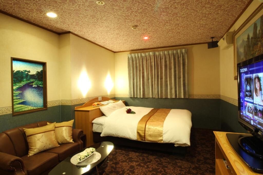 A hotel room with a bed, a sofa, a television, and a painting on the wall.