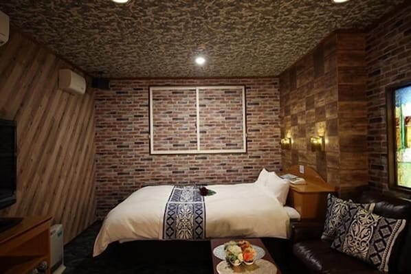 A room with a brick wall, a bed with a patterned bedspread, a leather sofa, and a television.