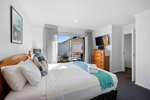 Ein Hotelzimmer mit Bett, Kommode, Fernseher und einer Glastür zum Balkon.