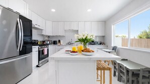 Een moderne keuken met witte kasten, een roestvrijstalen koelkast, een ontbijtje met croissants en fruit, en uitzicht op de omgeving.