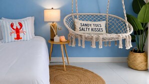 Een slaapkamer met een bed, een hangstoel met kussen, een nachtkastje met lamp en een kamerplant.