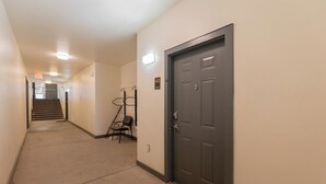 A hallway with a carpeted floor, a door with a number plate, a chair, and a coat rack.