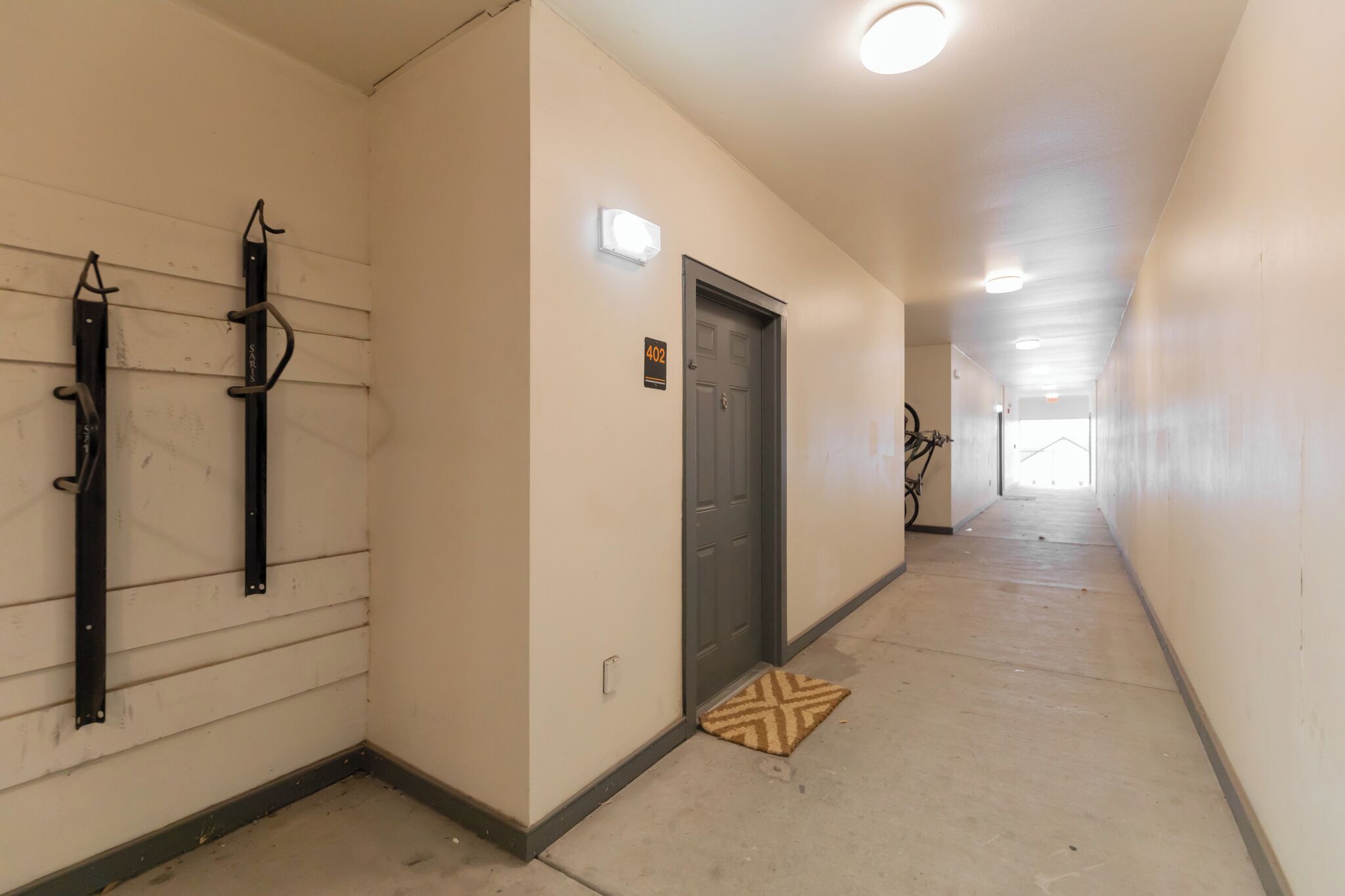 A hallway with a door marked '402,' a light fixture above it, and a doormat on the floor.