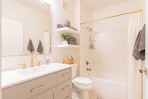 Un baño con lavamanos blanco, grifos dorados, inodoro blanco, bañera y cortina de ducha.