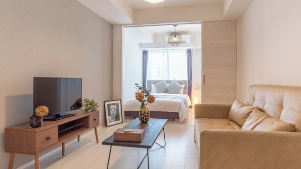 Ein modernes Schlafzimmer mit Bett, Fernseher, Sofa und Schreibtisch mit Vase und Bilderrahmen.
