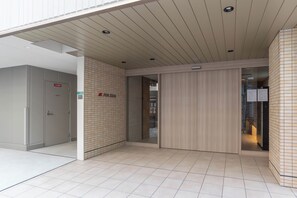 A modern hotel entrance with a tiled floor, a wooden panel wall, and a glass door leading to the interior. - FDS ZEAL (Osaka)
