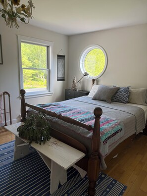 A bedroom with a bed, bedside table, lamp, window, and a view of greenery outside. - Serene 4-bedroom house with water access in charming Phippsburg (Phippsburg)