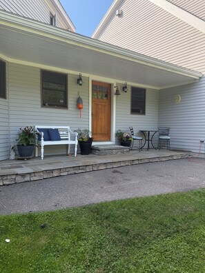 A house with a porch, a wooden door, a white bench, potted plants, and a small table with chairs. - Serene 4-bedroom house with water access in charming Phippsburg (Phippsburg)