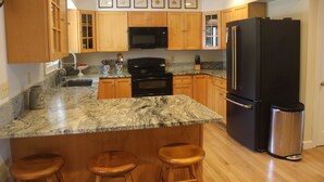 A kitchen with wooden cabinets, a black refrigerator, a stainless steel trash can, and a granite countertop. - Serene 4-bedroom house with water access in charming Phippsburg (Phippsburg)
