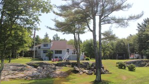 A house with a red roof, a flagpole, and a dock extending into a body of water. - Serene 4-bedroom house with water access in charming Phippsburg (Phippsburg)