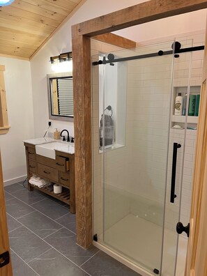 Une salle de bain moderne avec une douche Ă parois de verre, un meuble-lavabo en bois et un carrelage au sol.