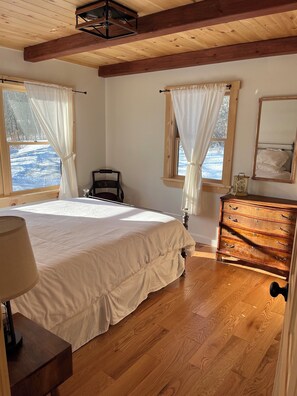 A bedroom with a wooden floor, a bed, a dresser, a chair, and a window with curtains. - 3-bedroom chalet in with mountain views, walking paths and private swimming pond (Margaretville)