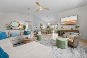 A spacious living room with a large sofa, a dining area, and a ceiling fan. - Waterfront Oasis - Heated Pool, Kayaks + Game Room (Palm Coast)