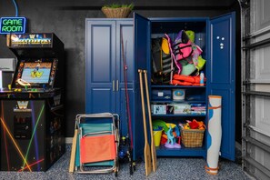 A room with a gaming machine, a blue wardrobe, and various sports equipment. - Waterfront Oasis - Heated Pool, Kayaks + Game Room (Palm Coast)