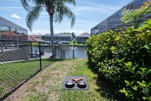 A fenced outdoor area with a water feature, a palm tree, and a table with bowls and a toy. - Waterfront Oasis - Heated Pool, Kayaks + Game Room (Palm Coast)