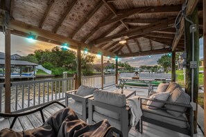 A covered outdoor seating area with wooden furniture and a view of a body of water. - Waterfront Oasis - Heated Pool, Kayaks + Game Room (Palm Coast)