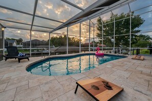 A covered outdoor swimming pool with lounge chairs, a wooden table, and a pink inflatable float. - Waterfront Oasis - Heated Pool, Kayaks + Game Room (Palm Coast)