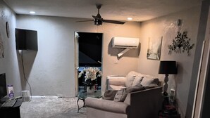 Una sala de estar con un sofá, un televisor, un ventilador de techo y una pequeña mesa con una planta.