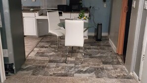 Cocina compacta con armarios blancos, microondas y un pequeño comedor con mesa de vidrio y dos sillas.