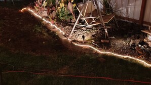 Un jardín con un arenero, un banco de madera y una guirnalda de luces a lo largo de un camino.