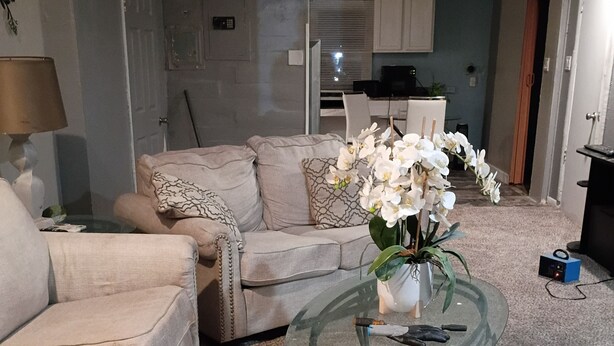 Una sala de estar con un sofá color beige, una mesa de centro de vidrio y orquídeas blancas.