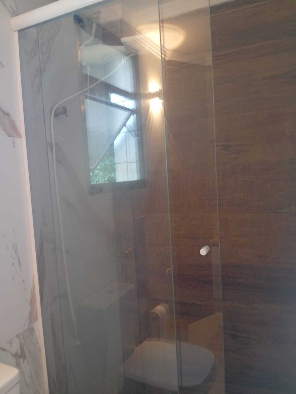A glass-enclosed shower area with a small window, a towel, and a toilet.