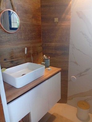 A bathroom with a wooden vanity, a white sink, a round mirror, and a marble wall. - Beachfront property with two oceanfront balconies (São Vicente)