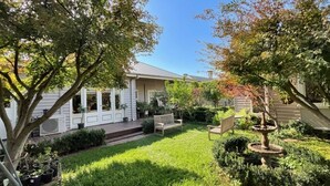 A residential backyard with a wooden deck, a garden with various plants, a wooden bench, and a birdbath. - Crofton House @ Port of Echuca - Heritage (Echuca)
