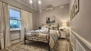 A bedroom with a four-poster bed, a nightstand with a lamp, a painting on the wall, and a window with curtains. - Crofton House @ Port of Echuca - Heritage (Echuca)