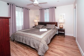 Quarto com uma cama grande, duas mesas de cabeceira com abajures, um ventilador de teto e piso de madeira.