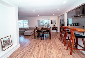 A spacious living area with a dining table, chairs, a sofa, and a kitchen in the background.