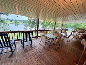 Eine überdachte Terrasse im Freien mit Holzboden, Metallstühlen, einem Tisch und Blick auf einen See.