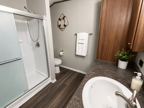 Une salle de bain Ă©quipĂ©e dâune douche, de toilettes, dâun lavabo et de meubles en bois.