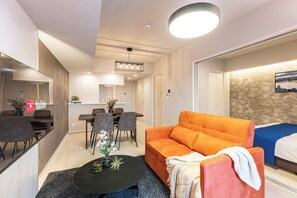 A modern hotel room with a sofa, a dining table with chairs, a kitchen area, and a bed. - FDS AURA (Osaka)