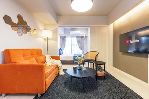 Ein modernes Hotelzimmer mit Sofa, Couchtisch, Fernseher und einem Bett mit Vorhängen.