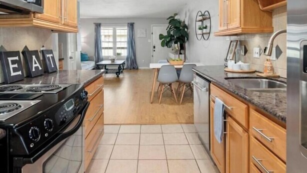 A kitchen with wooden cabinets, a stove, and a dining area with chairs and a table. - World Cup Ready 2BR Near NRG Stadium Skip the Parking (Houston)