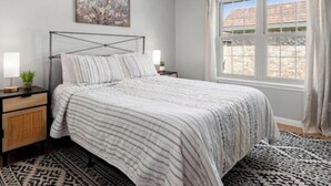A bedroom with a bed, bedside tables, a window with curtains, and a wall-mounted painting. - World Cup Ready 2BR Near NRG Stadium Skip the Parking (Houston)