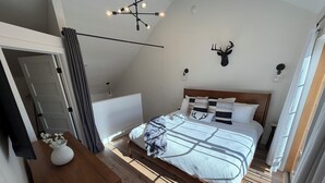 Un dormitorio con cama, cabeza de venado montada en la pared, lámpara de araña y suelo de madera.