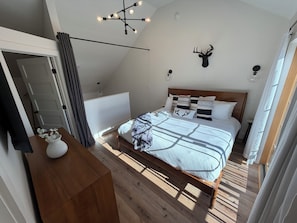 Un dormitorio con cama, cabeza de venado montada en la pared, lámpara de araña y suelo de madera.