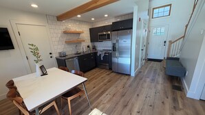 Una cocina moderna con armarios oscuros, electrodomésticos de acero inoxidable y una mesa de comedor de madera con sillas.