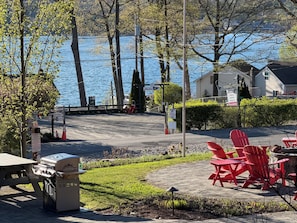 Un patio junto al lago con sillas Adirondack rojas, una parrilla y vista al agua.