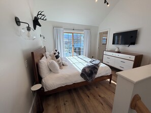 Un dormitorio con cama, cómoda, televisor y ventana con cortinas.