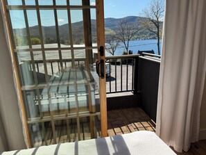 A balcony with a view of a lake and mountains, a wooden door, and a white curtain.