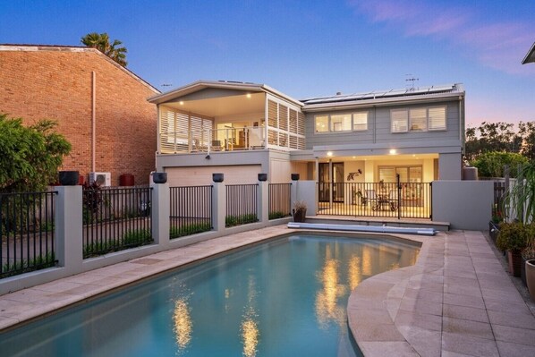 A two-story house with a swimming pool, a fenced backyard, and a balcony with outdoor furniture.