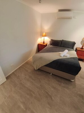 A bedroom with a bed, a nightstand with a lamp, a dresser, and a wall-mounted air conditioner. - WaterFront With Panoramic Views: Sunrise and Sunset (Chittaway Point)