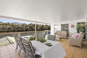 A dining area with a table set for four, chairs, a sofa, and a potted plant. - WaterFront With Panoramic Views: Sunrise and Sunset (Chittaway Point)